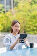 © StockPhotoRepublic - Beautiful Asian Woman Wearing Earbuds Using Tablet Outdoors a Greenery Office Building