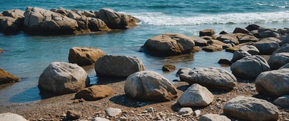 Poster - rocky shoreline with large boulders and gentle waves in clear blue sea under bright sunlight