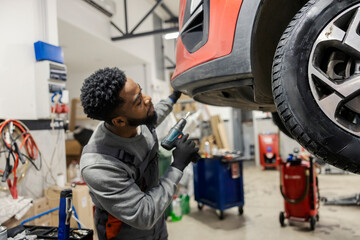 Fototapete - Hardworking black auto mechanic fixing car at auto mechanic workshop.