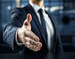 © Suchada - A businessman in a dark suit and tie extends his hand for a handshake, symbolizing partnership, agreement, and professional relationships.