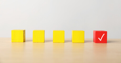 One red cube with check mark among others on table