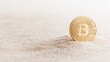 © Hryhor Denys - A gold cryptocurrency coin sits on a sandy surface, symbolizing the rise of digital currencies and their impact on financial investments in today's economy
