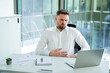 © RomArt production - A professional male in a formal setting holds his stomach, displaying discomfort while working, surrounded by modern office furnishings and documents on the desk for a corporate look.