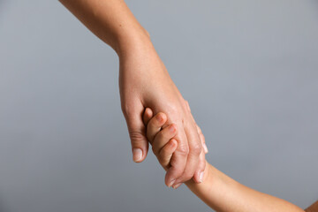 Wall Mural - Mother and child holding hands on grey background, closeup