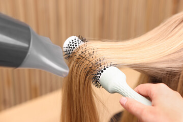 Wall Mural - Hairdresser styling client's hair with round brush and hairdryer in salon, closeup