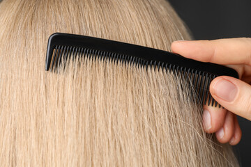 Wall Mural - Woman brushing hair with plastic comb on dark background, closeup