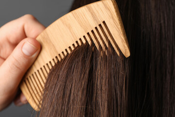 Wall Mural - Woman brushing hair with wooden comb on grey background, closeup