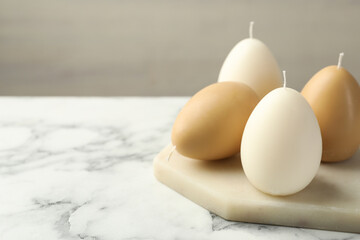 Wall Mural - Egg-shaped candles on white marble table against light gray background, closeup and space for text. Easter decor