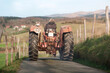 © Larraend Fotografía - Woman farmer driving old red tractor on a country road near farm and mountains, celebrating international workers' day
