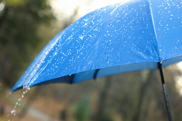 Wall Mural - Open blue umbrella under pouring rain outdoors, closeup