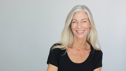 Wall Mural - A joyful woman with long gray hair and bright eyes smiles at the camera, showcasing a natural and cheerful demeanor in a calm setting