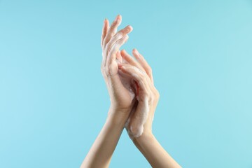 Wall Mural - Woman washing hands with foaming soap on light blue background, closeup. Hygiene