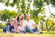 © Wanwajee - White happy family sitting on green yellow grass ground at park. Father, mother and daughter spent time together, looking away at public park.