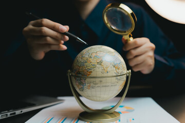 Poster - Person Holding Magnifying Glass Over Globe with Financial Charts Nearby