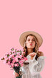 © HBS - Vertical image with free space. Portrait of a beautiful young woman in a beige spring dress and hat holding a bouquet of pink flowers and sending an air kiss to the camera. Concept of spring, beauty.