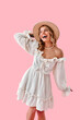 © HBS - Vertical image of a beautiful stylish modern happy smiling young woman wearing a beige ruffled dress and hat posing at the camera on a pink background. Style, fashion and shopping.