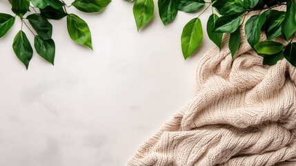 A cozy blanket lies beside a vibrant plant on a clean white surface, creating a serene and inviting atmosphere.