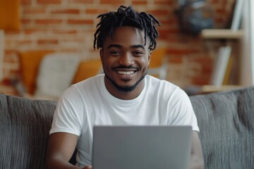 Freelance concept. Cheerful black man sitting on sofa, typing on laptop keyboard and smiling, guy working from home, copy space