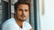 © JO BLA CO - A young man with chiseled features and styled hair sits relaxed outside a contemporary structure. Sunlight highlights his confident expression and casual attire, creating a striking image