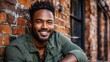 © JO BLA CO - A man exudes confidence and joy while leaning against a textured brick wall. His casual outfit and bright smile suggest a relaxed atmosphere on a sunny afternoon