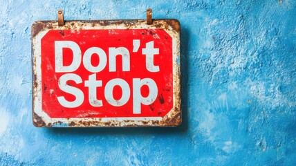 Red sign with Don't Stop message displayed on a textured blue wall in a contemporary urban setting