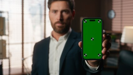 Portrait in office serious business specialist middle-aged Caucasian man businessman worker male guy holding mobile phone with green screen template chroma key mock up showing smartphone display app