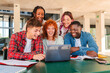 © Jose Calsina - Group of university students collaborating on homework together in a library, sharing ideas, using a laptop, studying with books and notes, showcasing teamwork, learning, and academic dedication