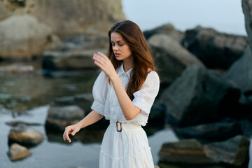 Poster - Majestic woman in flowing white dress standing with arms raised on picturesque rocky beach