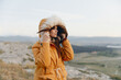 © SHOTPRIME STUDIO - Woman in orange parka standing on hill overlooking valley and mountains in travel adventure scene