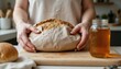 © Nathaphat - Handheld Freshly Baked Bread on Wooden Board with Glass Jar of Honey in Modern Kitchen Setting