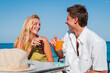 © Jose Calsina - Joyful Couple Enjoying Refreshing Drinks While Playfully Toasting Each Other At The Beachside Table On A Bright Sunny Day With Laughter And Smiles Illuminating Their Faces And Hearts Full Of Happiness