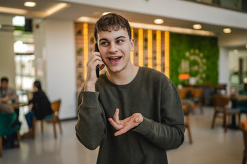 Wall Mural - young man student standing in a cafe and talk on mobile phone