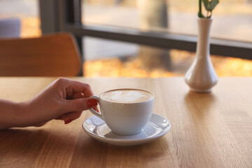 Wall Mural - Woman with cup of aromatic coffee at wooden table in cafe, closeup