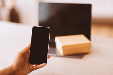 Poster - Technology Concept. Unrecognizable black woman holding and showing smartphone with blank empty screen for mock up. Laptop computer with present box or delivery package on keyboard in the background