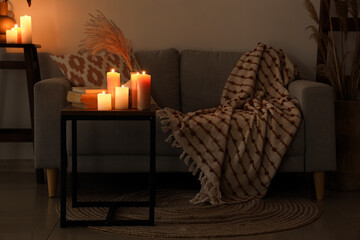 Wall Mural - Burning candles, vase with pampas grass and books on table in dark living room interior