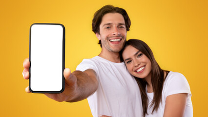 Poster - Using Cool Application. Portrait of cute millennial couple holding smartphone with white screen in hand, recommending mobile app, advertising your website, hugging, mock up for design. Selective focus