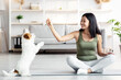 © Prostock-studio - Cheerful young asian woman in sportswear sitting on yoga mat and playing with her funny dog jack russel terrier breed while exercising at home, giving puppy treats, living room interior, copy space