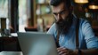 © KOSHKAROV SERGEI - Serious businessman with a beard focused on laptop in café