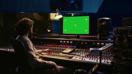 Fototapete - Tracking engineer watching tutorials online to learn mixing and mastering techniques, greenscreen display on pc and processing sounds. Artist technician operates control room switchers. Camera B.