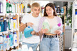 © JackF - Cheerful young couple trying to make choice between liquid laundry soaps in supermarket