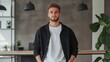 © Lifestyle Images - Young man standing in a modern office or workspace. he is wearing a black jacket over a white t-shirt and has a beard.