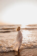 © Cavan Images - Woman in a flowing white dress standing in ocean waves at sunset