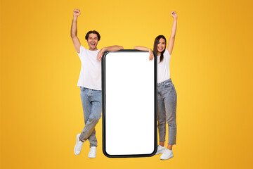 Poster - Wow, Great News. Full Body Length Of Cheerful Man And Lady Leaning On Big Smart Phone With Blank White Screen Shaking Clenched Fists, Celebrating Victory, Standing At Yellow Studio, Mock Up Collage