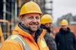 © Rizal - A portrait of smiling construction workers wearing yellow hard hats and orange safety jackets, standing in front of an industrial building site.
