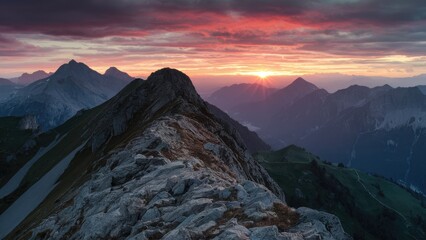 Wall Mural - Serene sunset over majestic mountain peaks with vibrant red and orange hues filling the sky and rocky foreground illuminated by the fading light