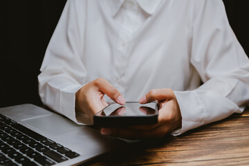 Poster - Hands Holding Smartphone Next to Laptop on Wooden Desk