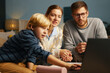 © DragonImages - Multiracial family gathered on couch, watching movie on laptop, family interaction, bonding, and quality time being spent together in comfortable living room setting