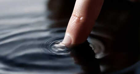 Poster - Close-up of finger touching water surface creating ripples on black background. Blue and black color. Focus on detail