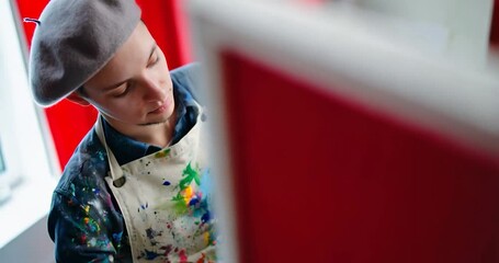Poster - Artist Painting on Canvas in a Studio with Paint Splatters on Clothes Red Wall and a White Background