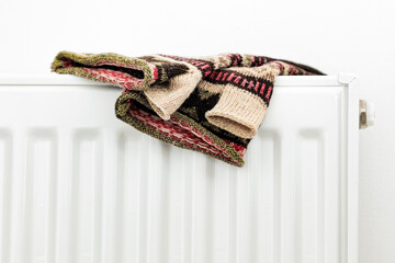 A pair of colorful knitted fingerless mittens drying on a white radiator, creating a cozy winter atmosphere. The wool texture and traditional pattern evoke warmth, home comfort, and seasonal coziness